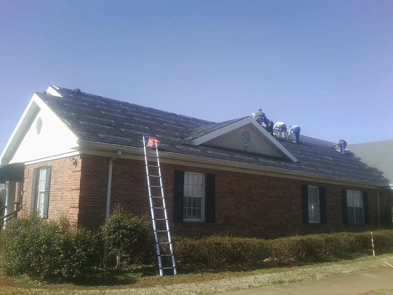 Crew tearing shingles off a brick ranch roof with a ladder set — Metal Roof Repair work by our crew in Donalsonville