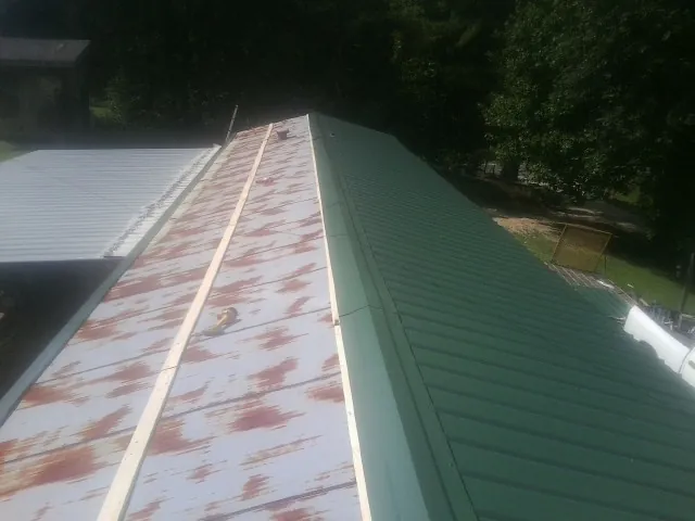 Old rusted panels beside newly installed green metal roofing — Wind Damage Roof Repair by Roofing Brothers in Donalsonville
