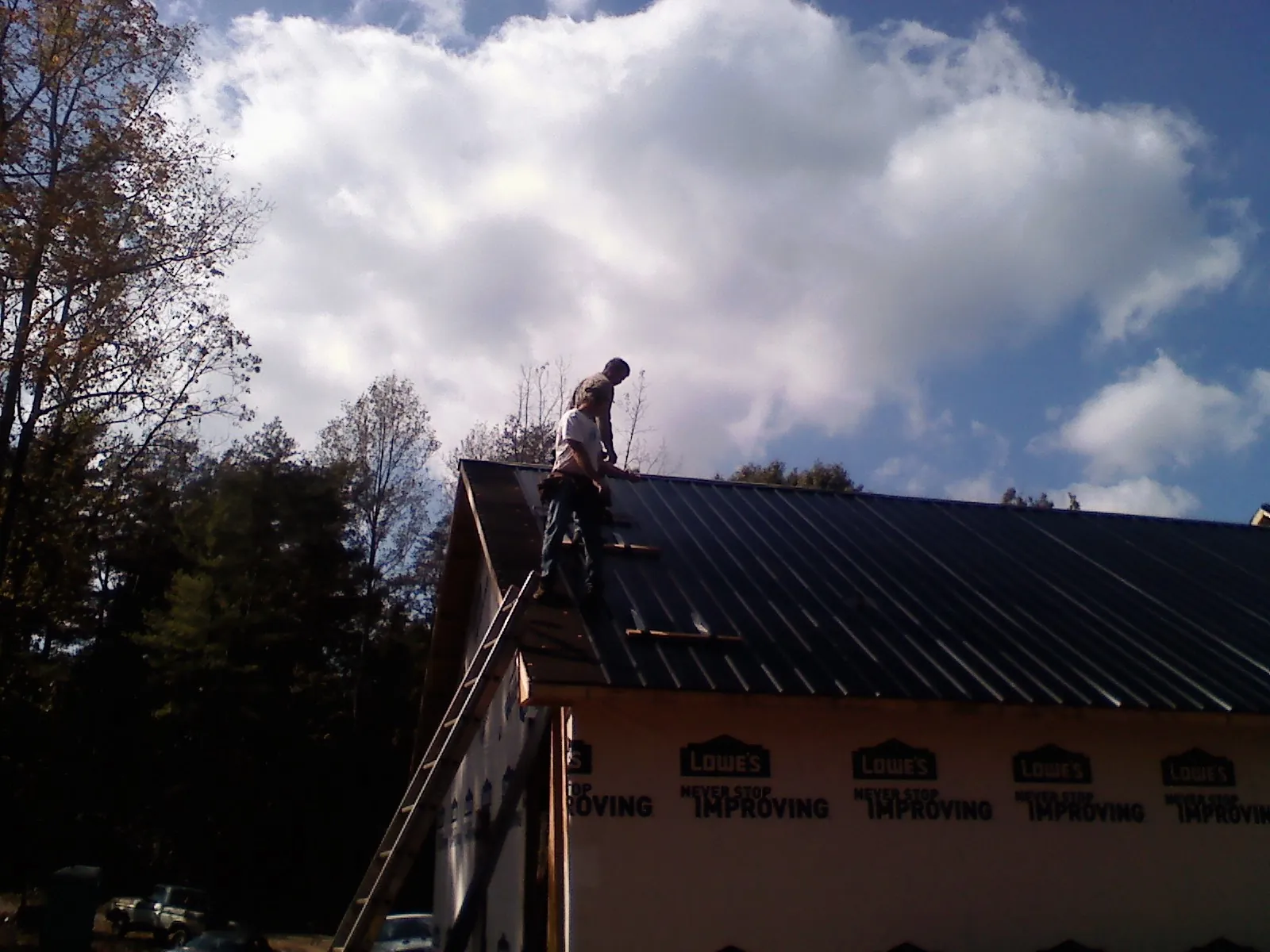 Roofer fastening dark metal panels high against a cloudy sky, from a Roof Inspection job in Donalsonville