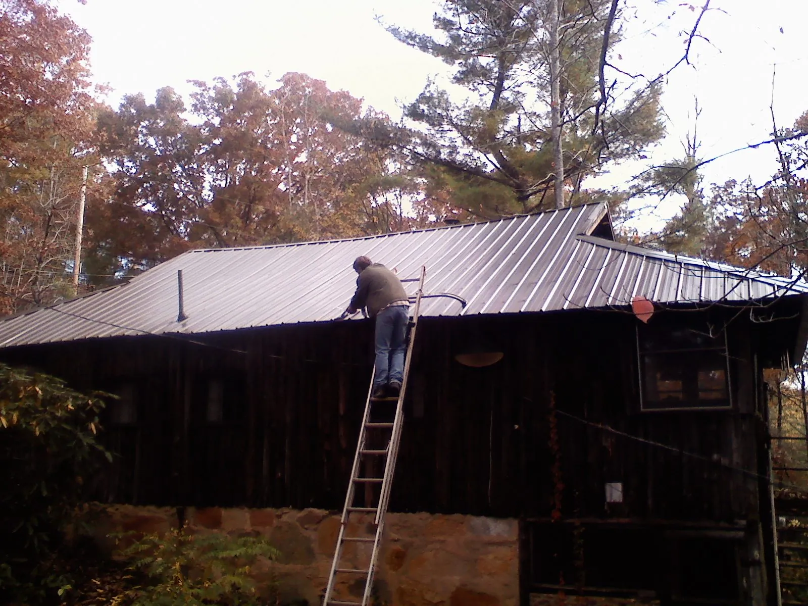 Roofer on a ladder working along the edge of a cabin metal roof in Donalsonville