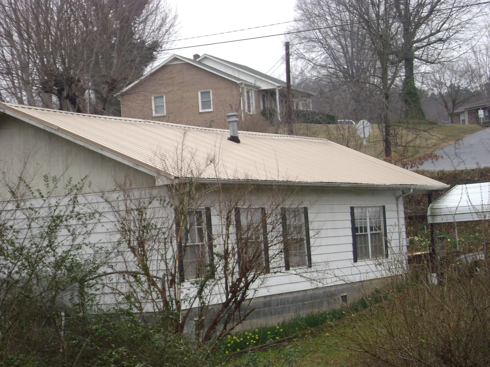 Tan metal roof on a white sided house set into a hillside — Commercial Roofing by Roofing Brothers in Donalsonville